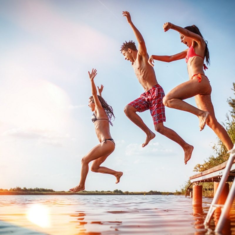 Group of friends jumping into the lake from wooden pier.Having f